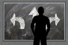 silhouetted person looking at blackboard with arrows pointed in different directions 